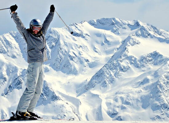 joyful female skier rising her hands up at mountain background
